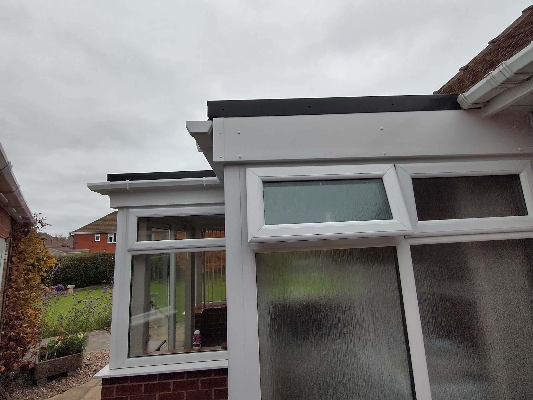 Conservatory with a new flat roof and white uPVC frames, seen from the garden
