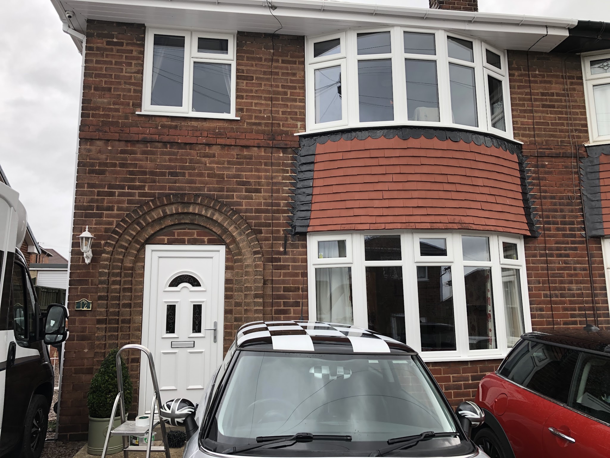 Red brick semi with white bay windows upstairs and down and a white front door