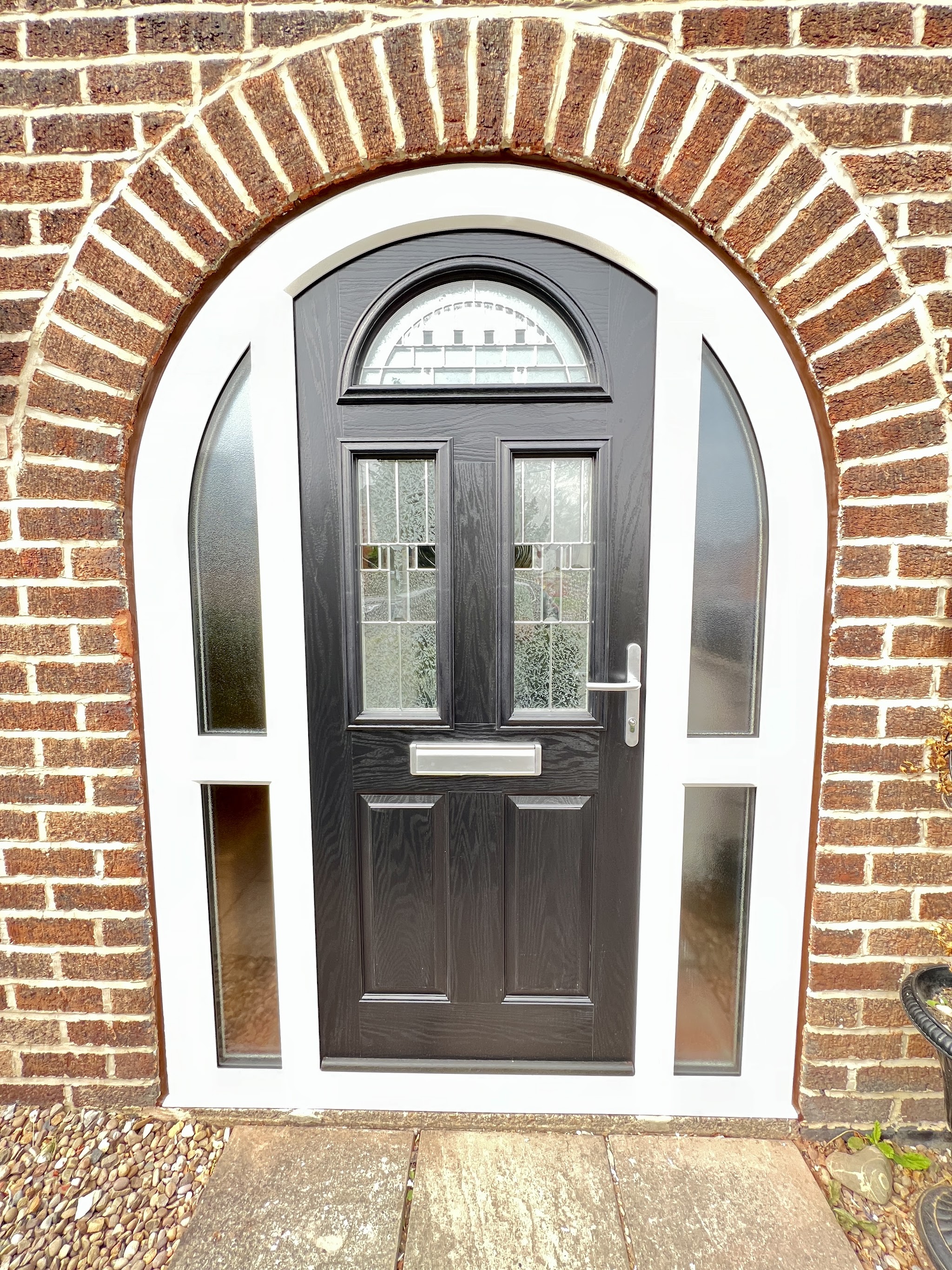 Close-up of a black arched composite door with glazed side panels in a brick arch